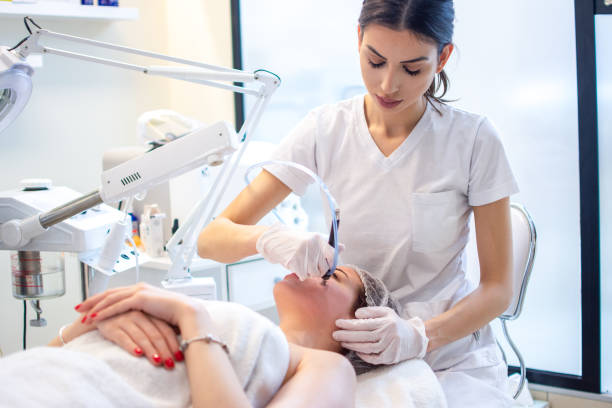 A woman receiving a facial treatment at a skincare clinic, with a female aesthetician wearing a white uniform using a professional device on her face.