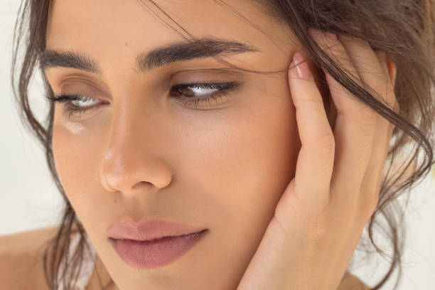 Close-up of a thoughtful young woman with a gentle expression, touching her temple, white background