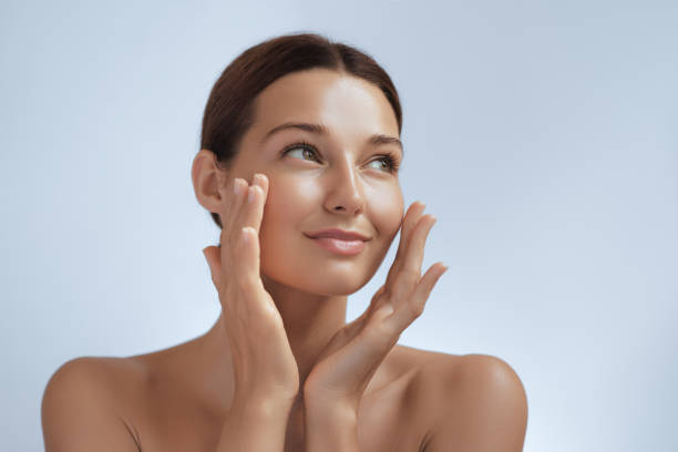 Portrait of a smiling woman applying facial cream and looking away