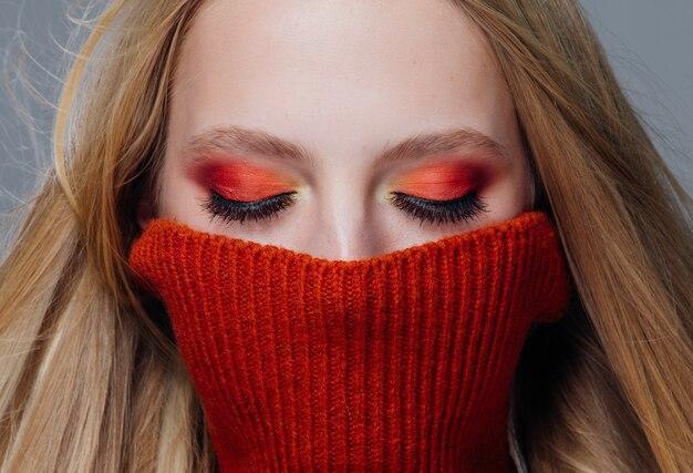 Woman with vibrant orange and yellow eyeshadow wearing a red turtleneck sweater